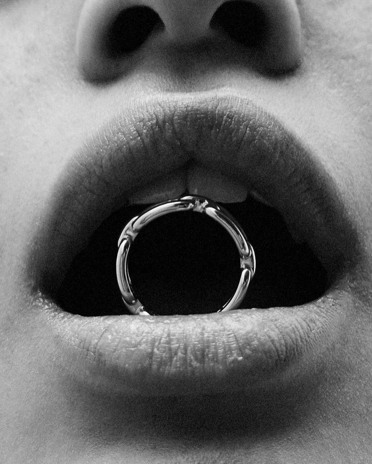 Black-and-white close-up of parted lips holding a polished ring